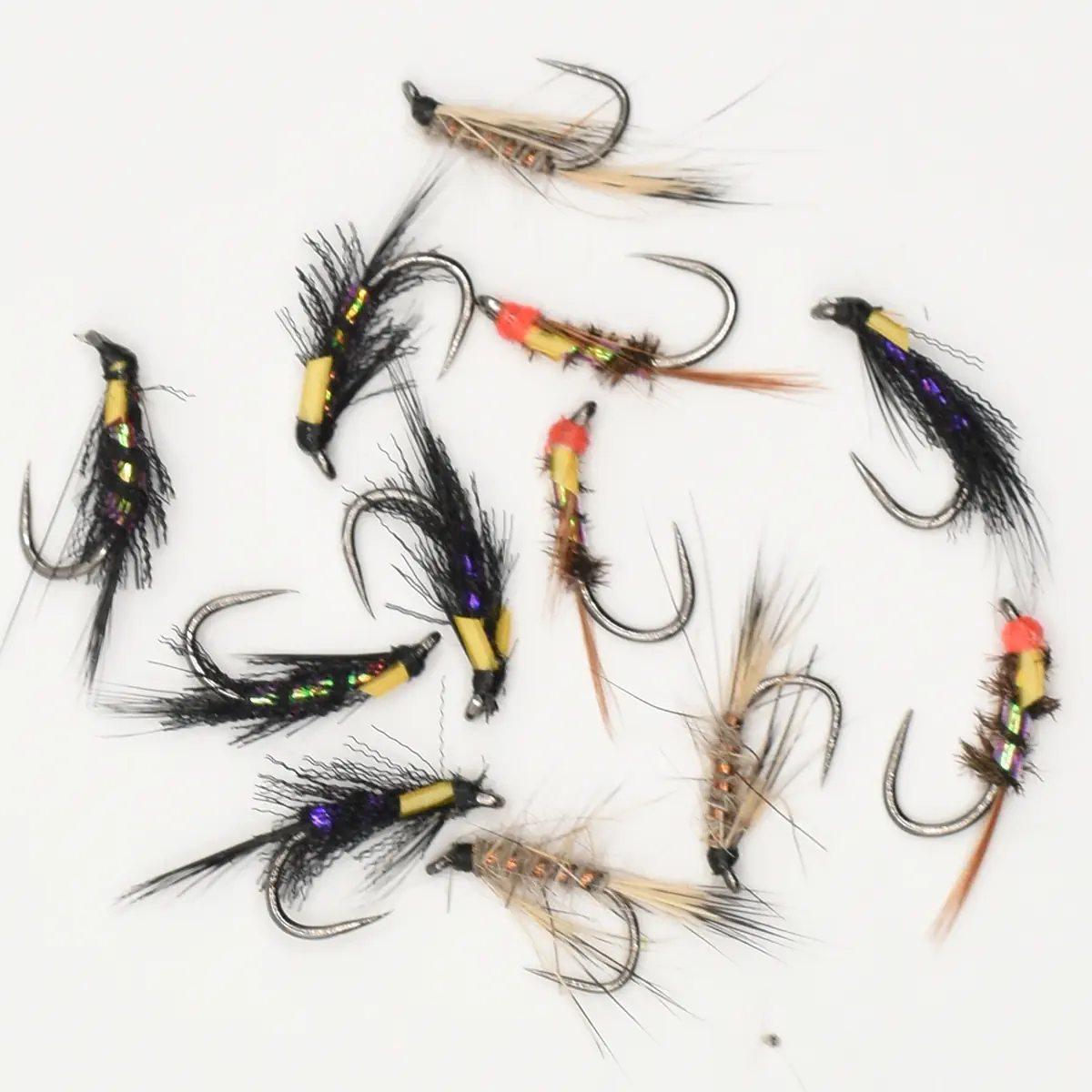 Assorted metallic and feather fishing flies laid out on a white background for fly fishing as lures