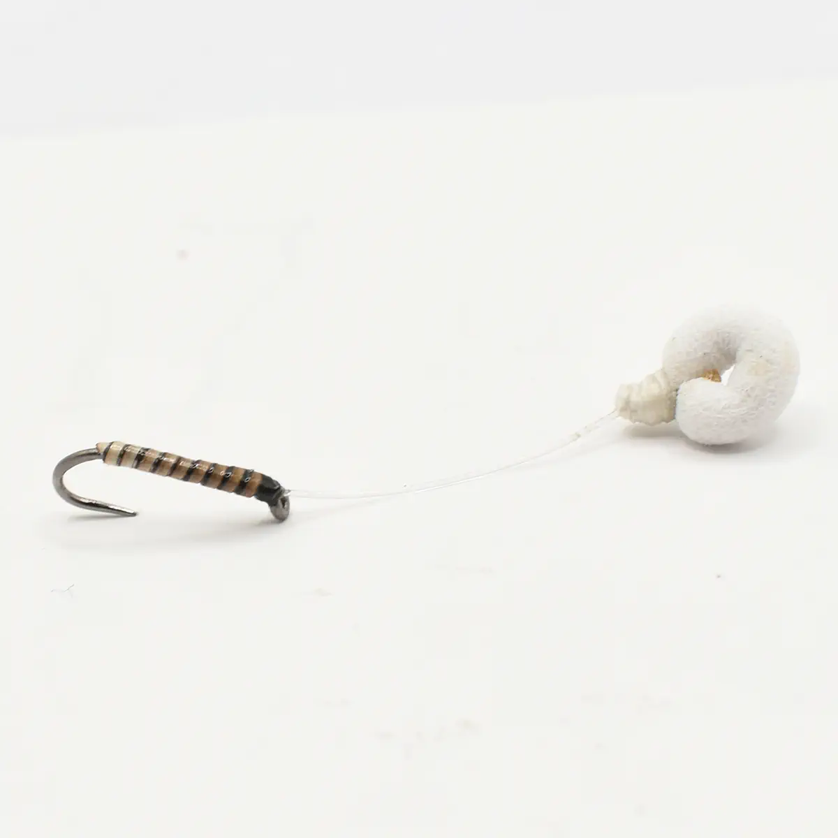 Small fishing lure with a curved hook, striped brown body, and a thin line leading to a white foam float on a white background.