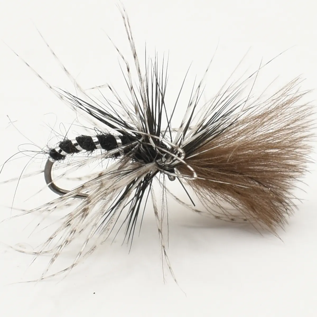 Close-up of a dry-fly fishing lure with a black body and brown-tan feather hackle on a curved hook surface, set against a light background.