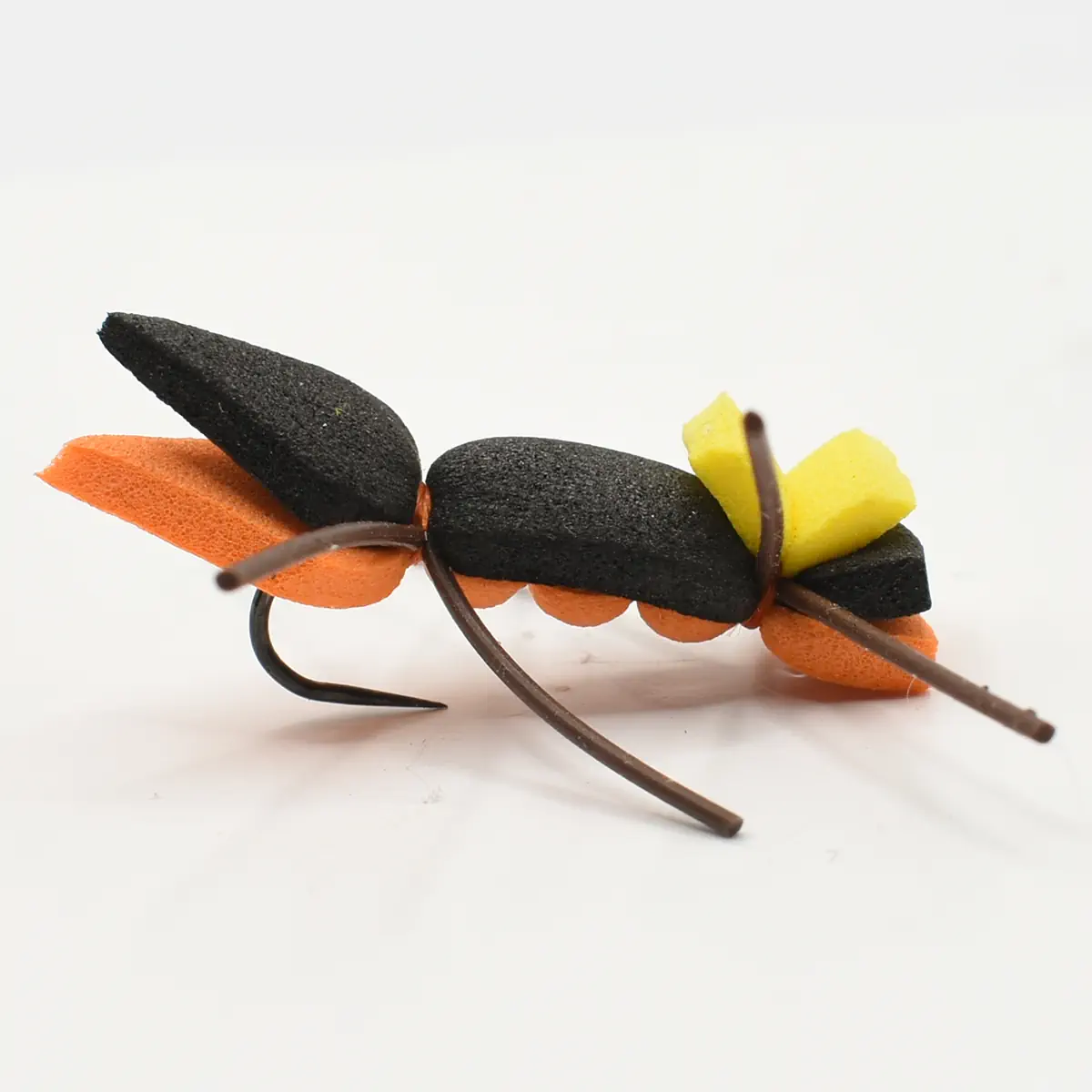 Close-up of an artificial fishing fly with a black and orange foam body and a yellow feather-like wing on a hook